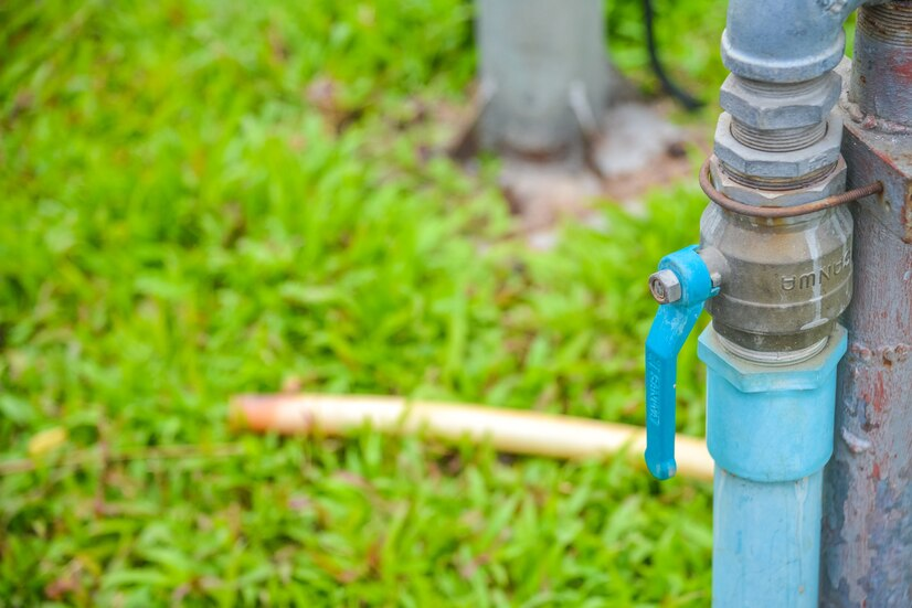 Valve faucet Outdoor water tap connected to a blue pipe, with a blurred green lawn background